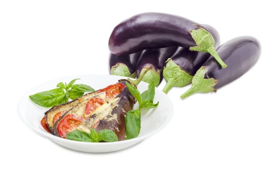 Baked eggplant stuffed with vegetables and cheese decorated with basil leaves on white dish on a background of a pile of the fresh eggplants on a white background
