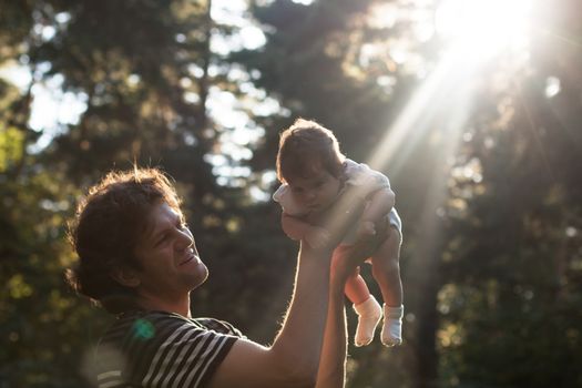 Happy joyful father having fun throws up in the air his child in the park in the evening - intentional sun glare and vintage color, lens focus on father. Father's day. Film filter.