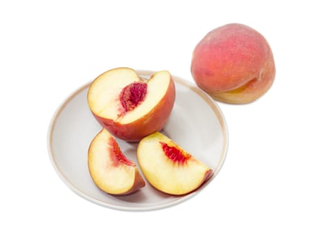 One whole ripe fresh peach and one cut into slices peach on a saucer on a white background
