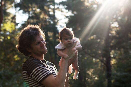 Happy joyful father having fun throws up in the air his child against the solar beam - intentional sun glare and vintage color, lens focus on father. Father's day. Film filter.