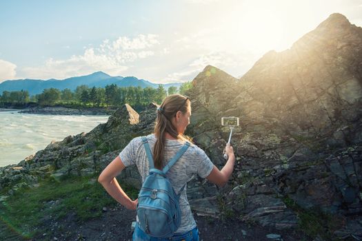 Woman taking selfie on mobile phone with stick. Vacation in the mountain