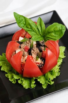 Festive appetizer. Tomato stuffed with chopped tuna salad, egg, tomato cubes, olive slices and the addition of capers, greens