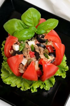 Festive appetizer. Tomato stuffed with chopped tuna salad, egg, tomato cubes, olive slices and the addition of capers, greens