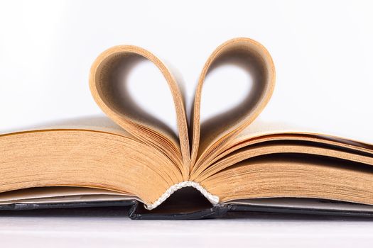 Pages of a book curved into a heart shape on white background