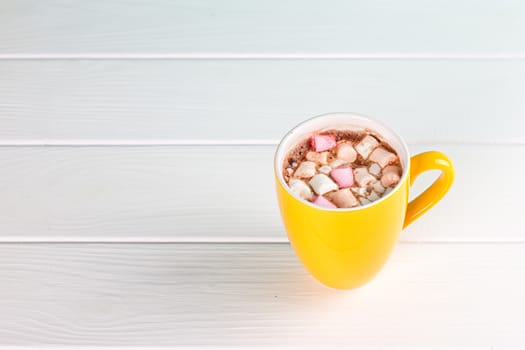 Yellow cup of hot cocoa with marshmallows on white wooden background