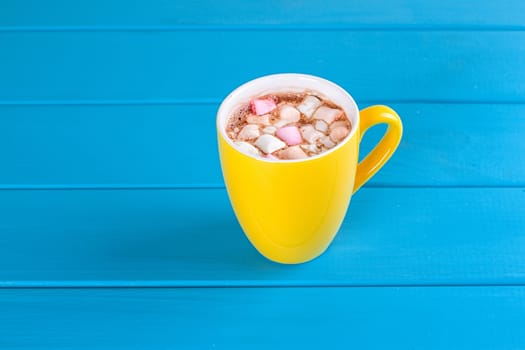 Yellow cup of hot cocoa with marshmallows on blue wooden background