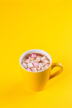 Yellow cup of hot cocoa with marshmallows on yellow background