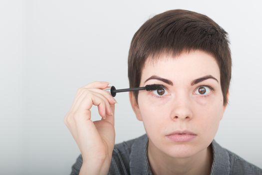 Beauty make-up. Portrait of young girl with fake eyelashes applying black mascara on lashes, holding brush in hand. Sexy female with soft skin and perfect makeup. Cosmetics.