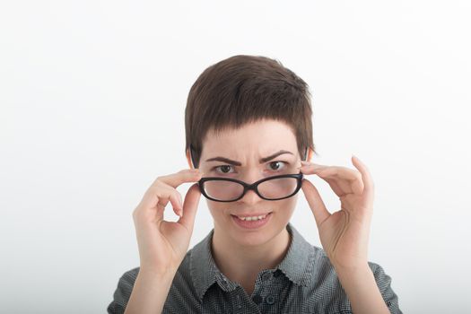 Young female teacher in a plaid shirt looking over her glasses on white background