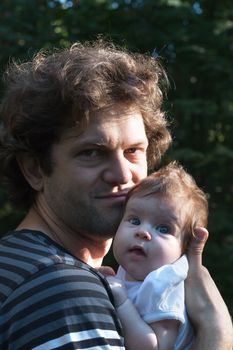 Dad is holding a daughter in his arms for a walk in the park. Spring day, family walk in nature, sunny.