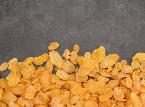 Corn flakes breakfast cereal in a border line with copy space on a dark grey slate tile background