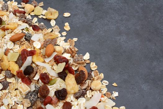 Muesli - cereal flakes with seeds, mixed fruit and nuts - in a diagonal line with copy space on a dark grey slate tile background