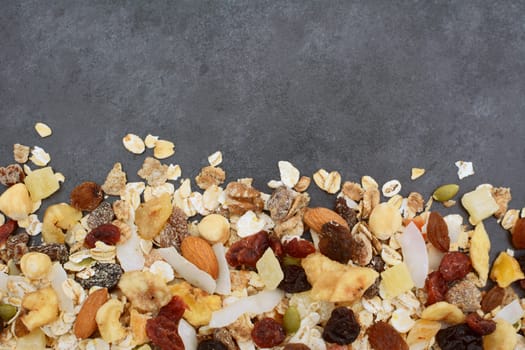 Muesli - cereal flakes with seeds, mixed fruit and nuts - in a border line with copy space on a dark grey slate tile background