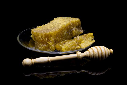 Honey with honeycombs on a glass plate on a black background