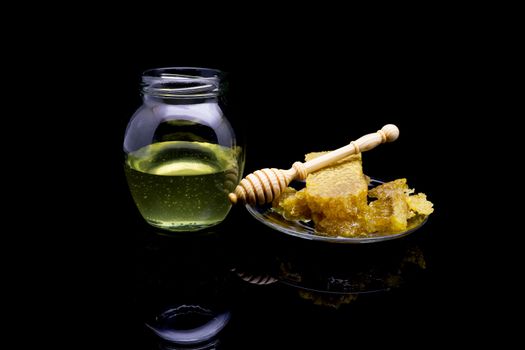 Honey with honeycombs on a glass plate on a black background