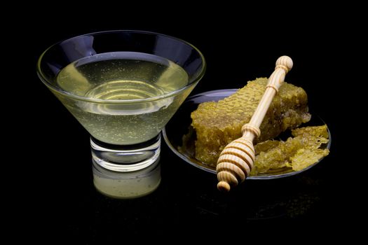 Honey with honeycombs on a glass plate on a black background