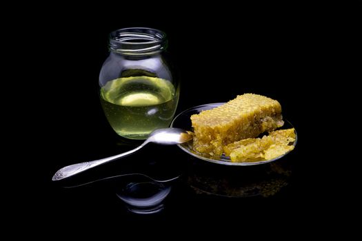 Honey with honeycombs on a glass plate on a black background