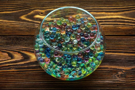Colored hydrogel balls in a glass vase on a wooden table