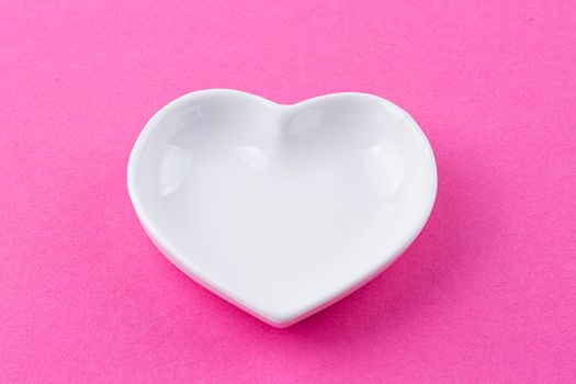 White plate in the shape of heart on a pink background