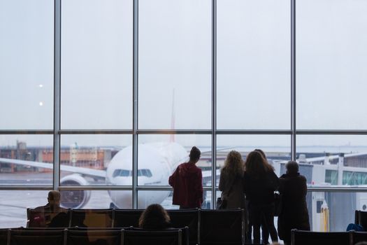 People waiting for airplane departure at the airport gates on a rainy day. Bad rainy weather with storms and strong winds causing delays in air traffic.