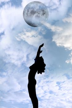 attractive silhouetted nude woman holding her hands up to the sky giving gratitude to the moon in a yoga pose with a cloudy background