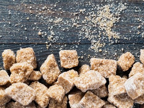 natural raw brown cane sugar cubes and granulated brown sugar on brown wooden background. Top view of brown sugar with copyspace