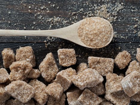 natural raw brown cane sugar cubes and granulated brown sugar in spoon close up as background. Top view of brown sugar