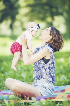 Young beautiful mother sits on blanket with her daughter during a picnic in the park