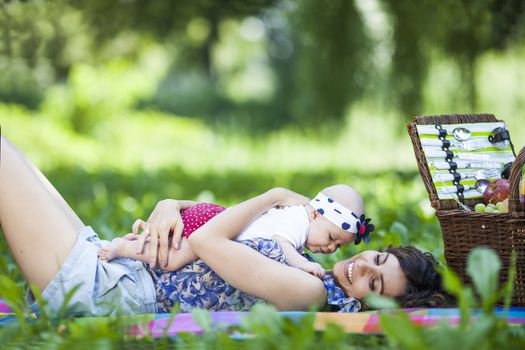 Young beautiful mother sits on blanket with her daughter during a picnic in the park