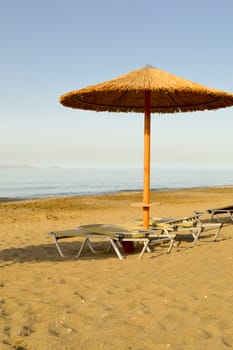 Sun loungers and umbrella on a sandy beach and a blue sky background on the island of Crete