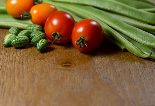 Cucamelons, orange and red tomatoes in selective focus against fresh green runner beans on wood with copy space