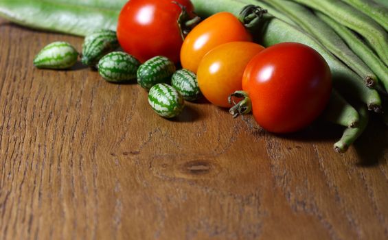 Cucamelons in selective focus with red and orange tomatoes, and green runner beans on wood with copy space