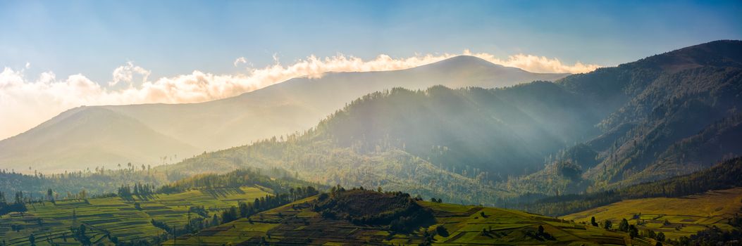 panorama of mountainous rural area at sunrise. Gorgeous autumnal morning weather with clouds above the mountains and fog in valley