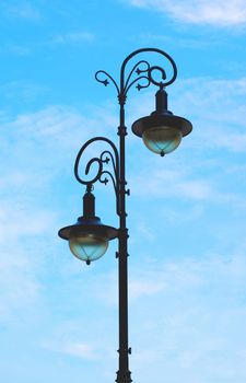 Elegant Street Lantern with with Forged Curled Details against Blue Cloudy Sky Outdoors