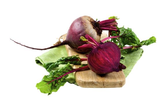 One Full Body Fresh Raw Organic Beet and Half with Green Beet Tops on Wooden Board and Napkin isolated on White background
