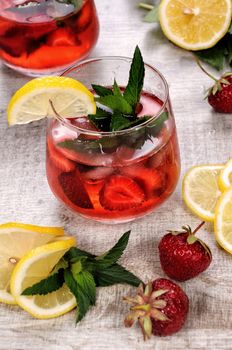 A glass of chilled strawberry lemonade, mint leaves, a slice of lemon with ice