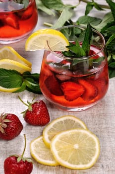 A glass of chilled strawberry lemonade, mint leaves, a slice of lemon with ice