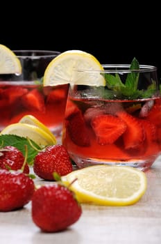 A glass of chilled strawberry lemonade, mint leaves, a slice of lemon with ice
