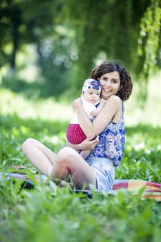 Young beautiful mother sits on blanket with her daughter during a picnic in the park
