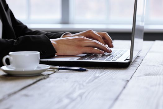 Man working on a laptop on a rustic wooden table, hands close up