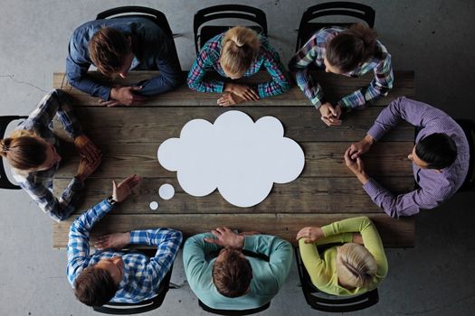 Hipster business teamwork brainstorming planning meeting concept, man tells his opinion, people sitting around the table with white paper shaped like dialog cloud