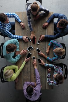 Team of business people in casual clothes sitting around the table, taking their mobile phones, top view