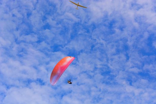Paramotor wing airman  and motorless flying with a glider against blue sky.