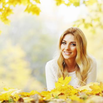 Young woman laying down on the ground covered dry autumnal foliage in beautiful park