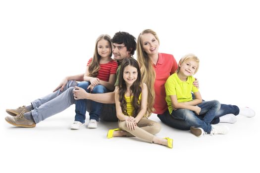 Happy smiling family of two parents and three children sitting on the floor studio isolated on white background