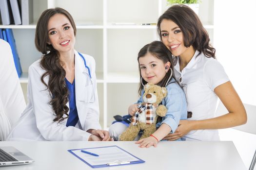 Happy mother and child with teddy bear and stethoscope at pediatrician office