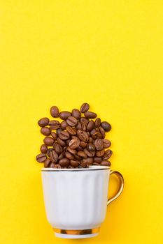 coffee beans spilled out of a cup on the yellowbackground