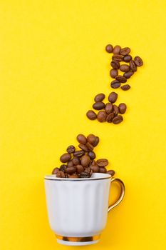 coffee beans spilled out of a cup on the yellowbackground