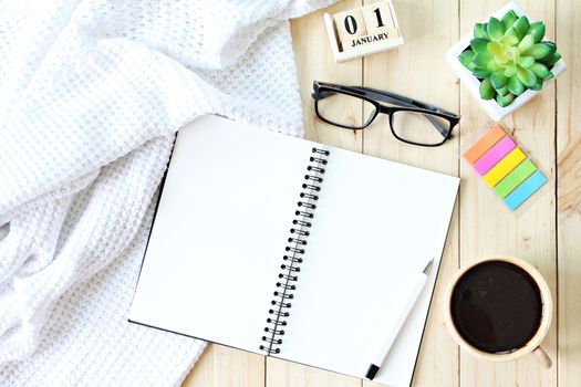 Business, weekend, holiday or new year planning concept : Flat lay or top view of  white knitted blanket, open blank notebook paper, coffee cup and new year cube calendar on wooden background