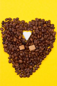 Coffee beans and sugar in the form of heart on a yellow background